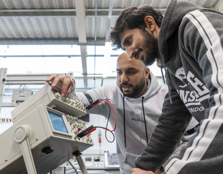 Two students working together on an oscilloscope, adjusting settings to analyze waveforms in an electronics engineering lab. Two students working together on an oscilloscope, adjusting settings to analyze waveforms in an electronics engineering lab.